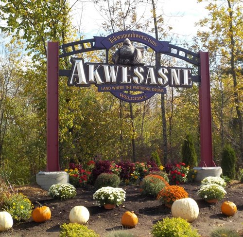 A photo of the entrance to Akwesasne, showing a sign and decorated with pumpkins and gourds.