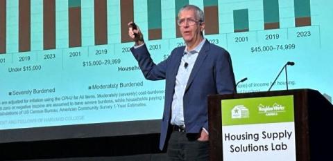 Chris Herbert presents keynote speech at Solutions Lab in front of a large graphic.