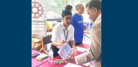 A woman stands behind a table, explaining the new Renaissance program to a business owner.