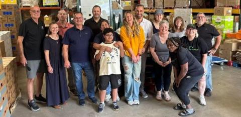 Volunteers in front of boxes in a warehouse with food and supplies.
